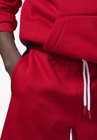 Sudadera roja de algodón con un bolsillo delantero tipo canguro. Combinada con pantalones deportivos rojos que tienen una cintura elástica y cordones blancos.