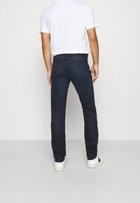 Mörkblå denimjeans med slim fit, i rak modell, bakfickor och minimala sömnadsdetaljer, bärs med en vit t-shirt.