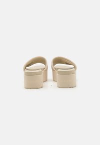 Beige platform sandals, featuring a smooth synthetic strap, rounded footbed, and embossed "Calvin Klein" logo on the heel.