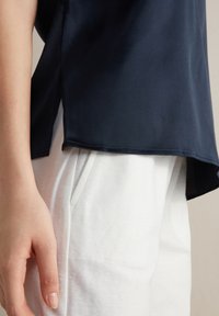  Marinblå satinblus med en avslappnad passform, med sidslitsar. Kombinerad med vita texturerade byxor, som visar en mjuk tygkontrast.