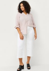 Light pink linen button-up shirt with rolled sleeves, paired with white wide-leg trousers and black platform mules. Simple and breathable design.