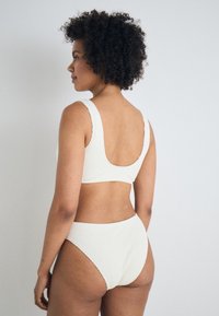 Ensemble de bikini côtelé de couleur crème comprenant un haut à dos en scoop et un bas taille haute, fabriqué à partir d'un tissu texturé avec de larges bretelles.
