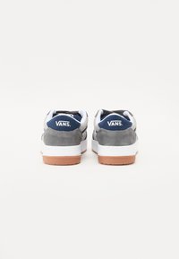 Ténis Vans em camurça cinza com detalhes brancos. Apresenta um emblema azul-marinho no calcanhar e uma sola de borracha gum. Design clássico de cano baixo.
