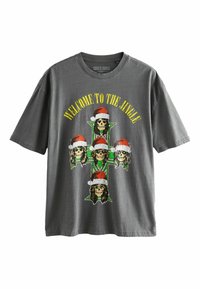 Szürke pamut póló, amelyen egy öt koponyát ábrázoló nagy grafika látható, amelyek Mikulás sapkát viselnek, egy zöld kereszt előtt, felettük a "WELCOME TO THE JUNGLE" felirat.