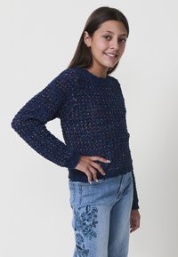 Maglione a maglia blu navy con un design testurizzato, colletto rotondo e polsini a coste. Abbinato a jeans azzurri chiari con ricami floreali.