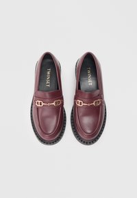 Bruna läderloafers med detalj i guld på hårdvara och tjocka svarta gummisulor. Slät textur, rund tå och en klassisk design.