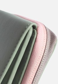 Vikbar plånbok i grön läder med rosa och ljusgrå tygdetaljer; har en mjuk yta och kontrasterande sömmar.