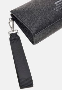 Czarna skórzana przyciągająca wzrok torba z zamkiem błyskawicznym, z odpinanym paskiem i tłoczonym logo. Smukły, prostokątny kształt.