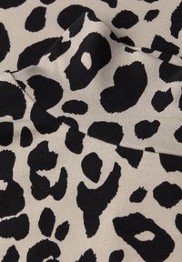 Látka s leopardím vzorem s béžovým pozadím a výraznými černými skvrnami, která se vyznačuje texturovaným, žebrovaným povrchem.