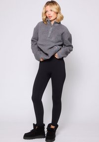 Pullover grigio in fleece con una cerniera argentata, leggings neri e stivali neri foderati in pelliccia. Il pullover ha maniche oversize e una vestibilità rilassata.
