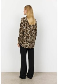 Halenka s leopardím vzorem, dlouhými rukávy, měkkou tkaninou a zakulaceným lemem, doplněná volnými černými kalhotami.