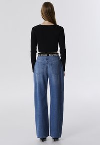 Haut noir à manches longues côtelé avec un col rond, assorti à un jean en denim bleu taille haute et jambes larges avec une ceinture de marque.