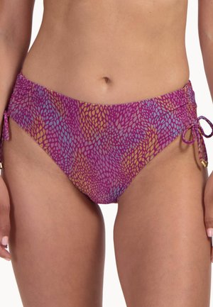 Vrouw die een paarse bikini onderbroek draagt met blauw-gele abstracte bladpatronen en zijkanten met verstelbare koordjes.