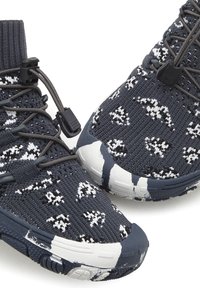 Sportliche Schuhe mit einem marineblauen und weißen Strick-Obermaterial, das ein strukturiertes Muster aufweist, synthetische Akzente hat und eine Gummisohle mit sichtbarem Verschleiß.