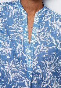 Camicia blu floreale con colletto alla mandarino, stampa botanica bianca e pantamolle senza bottoni, realizzata in tessuto leggero.
