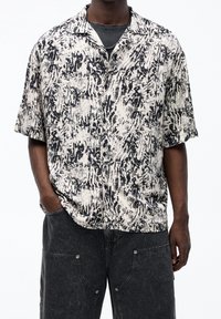 Camicia a maniche corte nera e crema con un audace motivo astratto, realizzata in tessuto leggero, dotata di colletto con bottoni e vestibilità rilassata.