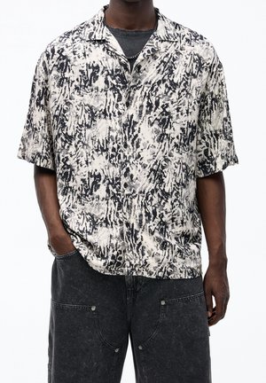 Camisa de manga corta en negro y crema con un audaz patrón abstracto, hecha de una tela ligera, que cuenta con cuello de botón y un corte relajado.