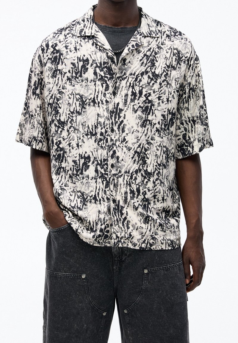Camicia a maniche corte nera e crema con un audace motivo astratto, realizzata in tessuto leggero, dotata di colletto con bottoni e vestibilità rilassata.