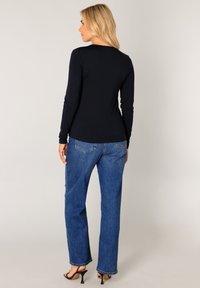 Marineblauwe longsleeve top gecombineerd met blauwe skinny jeans. De outfit heeft een getailleerde snit en een gladde textuur, aangevuld met hoge hakken.