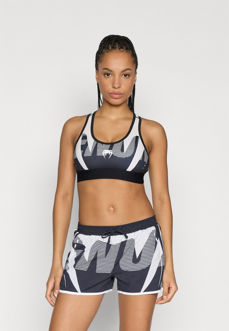 Conjunto de soutien desportivo e calções em preto e branco, com padrão gráfico. O soutien tem uma faixa sólida; os calções têm cintura elástica com cordão.