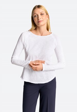 White long-sleeve shirt with a round neckline, lightweight and textured fabric, and a slightly curved hem, paired with dark pants.