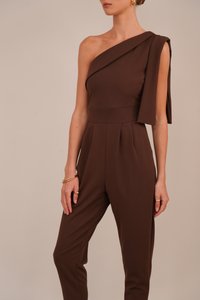 Smeđa kombinezon na jedno rame s drapiranom rukavom, prilagođenim gornjim dijelom i uskim nogavicama. Glatka tekstura, minimalne detalje i elegantna silueta.