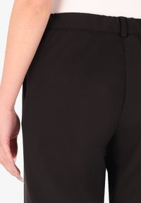 Pantaloni neri con una texture liscia e vita aderente, con un dettaglio di vita discreto e senza tasche visibili.