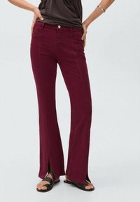 Jean flare bordeaux avec fentes sur les côtés, dotés de poches avant et d'une fermeture à bouton en métal. Fabriqué en denim au toucher lisse.
