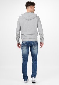 Grijze hoodie met een voorzak en een trekkoord, gecombineerd met blauwe vervaagde jeans met borduursel op de achterzak en witte sneakers.