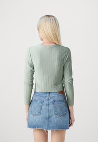 Grüner gerippter Langarmoberteil mit rundem Ausschnitt, kombiniert mit einem Jeans-Minirock mit fransigen Kanten und Gesäßtaschen.