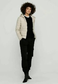 Beige quilted puffer jacket with a hood, black sweater beneath, and black cargo pants. Black heeled boots complete the outfit.
