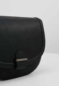 Borsa a tracolla in pelle nera con texture, dotata di un flap rotondo, chiusura in metallo argentato e dettagli di cucitura tono su tono.