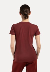 T-shirt bordeaux a maniche corte realizzato in tessuto morbido. Presenta un colletto rotondo e una silhouette aderente. Nessun motivo visibile o accessori.