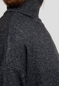 Maglione a collo alto grigio scuro con tessuto a maglia testurizzato, caratterizzato da un colletto alto e maniche raglan, che presenta una vestibilità rilassata e cuciture minime.