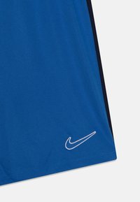 Camiseta deportiva azul hecha de tela suave, con un logo blanco de Nike y franjas oscuras a los lados. El diseño es simple y clásico.