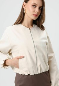 Licht crèmekleurig bomberjack met een ronde halslijn, ritssluiting, elastische manchetten en zijzakken. Gladde stof met een licht gestructureerde afwerking.