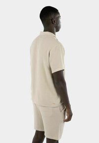 Beige teksturert kortermet skjorte og matchende shorts, med en avslappet passform. Skjorten har krage og et akzentlogo nær sømmen.