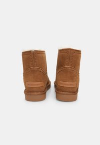 Botine din suede maro, cu o căptușeală moale albă, caracterizate prin detalii simple de cusătură și o talpă din cauciuc brown cu logo pe spate.