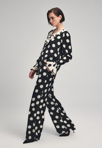 Zwart-witte outfit met polka dots, bestaande uit een losse blouse met een ruches halslijn en wijde broekspijpen, beide gemaakt van zachte stof.