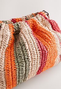 Sac tissé présentant des rayures orange, rouge, vert et beige. Fini texturé avec un sommet froncé et une sangle synthétique robuste.