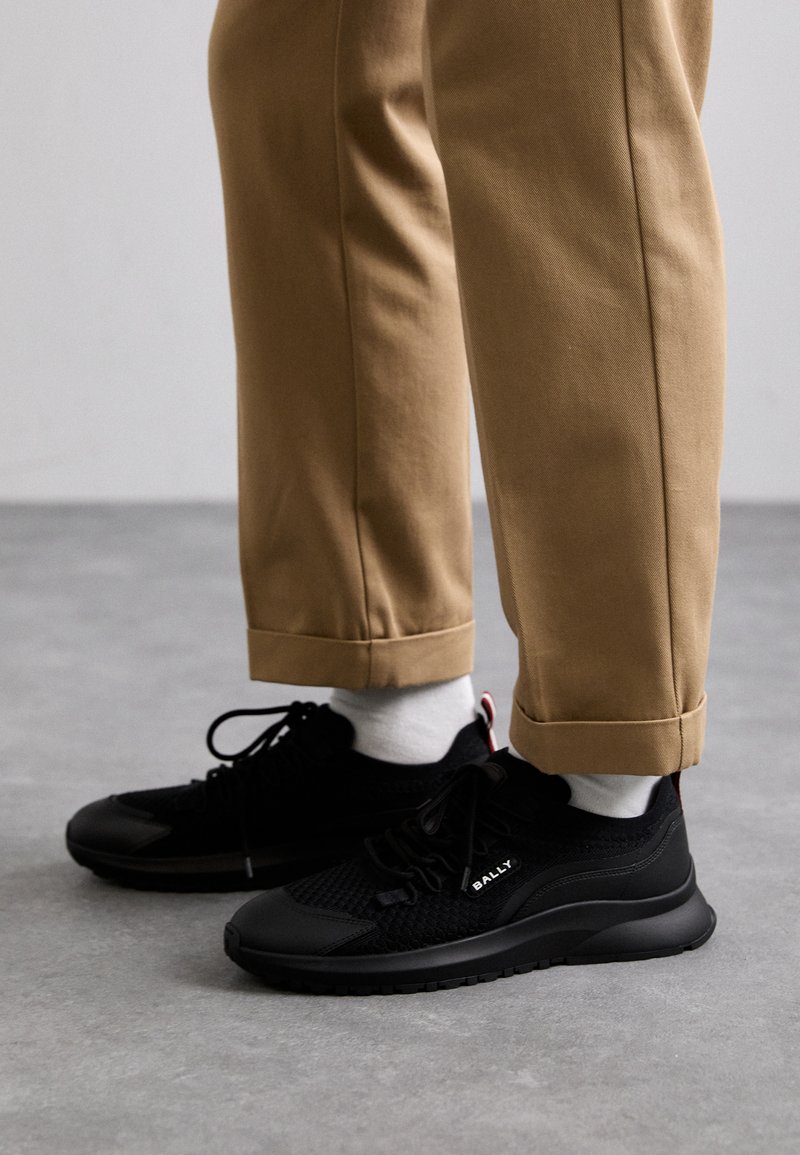 Scarpe sportive nere in rete e materiale sintetico con tomaia a trama, punta rotonda e suola piatta in gomma. Abbinate a pantaloni chiari con risvolto.