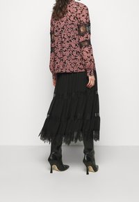 Jupe noire avec des volants en dentelle, assortie à un blouse à motifs floraux roses avec des manches en dentelle noire translucide. Bottes noires à talons.