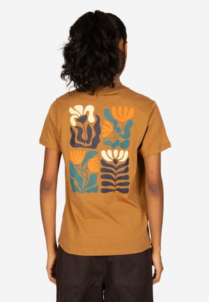 Person mit dunklem lockigem Haar im Pferdeschwanz trägt ein braunes T-Shirt mit abstraktem Blumenmuster in Orange, Blau, Weiß und Schwarz auf dem Rücken.