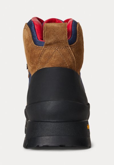 Stivale da trekking in suede marrone e tessuto blu navy con suola in gomma nera, rivestimento rosso e un'etichetta sul retro per indossarlo facilmente.