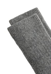 Calze di lana grigie con una texture a coste, caratterizzate da un design uniforme e un aspetto morbido e peloso. I bordi sono rifiniti con cura.