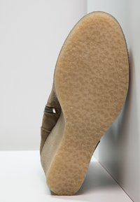 Suola di scarpa in pelle scamosciata marrone chiaro con suola esterna in gomma beige testurizzata. Presenta una forma curva e un decor minimalista lungo il lato.