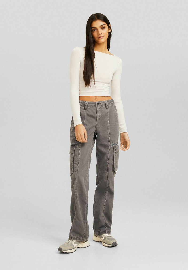 Grijze cargobroek met een relaxte pasvorm, voorzien van meerdere zijzakken en een knoopsluiting, gecombineerd met een wit slim-fit longsleeve shirt.