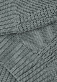 Gefalteter grauer Strickstoff, der im Nahaufnahme-Detail Rippen- und glatt rechts Muster zeigt.