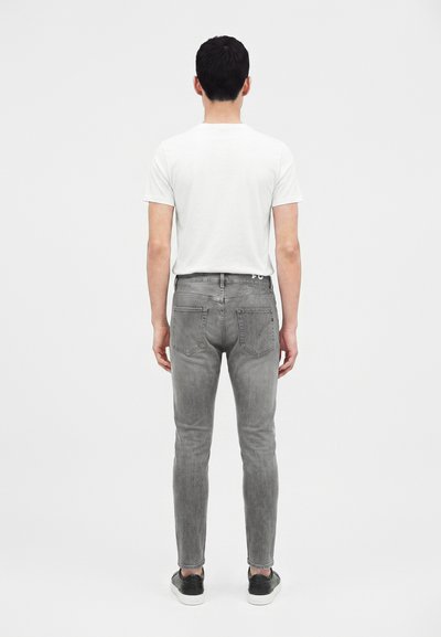 Homme debout de dos portant un t-shirt blanc uni à manches courtes, un jean skinny gris et des baskets noires avec des semelles blanches.