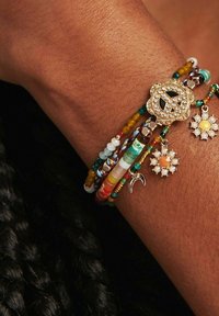 Bracelet en perles colorées comprenant des perles jaunes, vertes, orange et bleues, avec un symbole de paix en or, des charms floraux et des accents brillants.